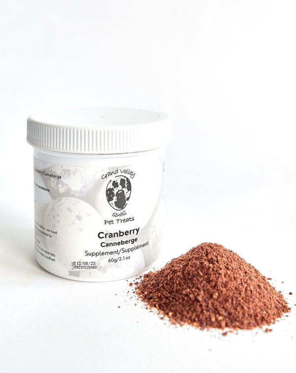 A white container of Grand Valley Quail Pet Treats cranberry supplement for dogs, placed next to a small pile of fine cranberry powder. The label highlights its natural ingredients and use as a dietary supplement.