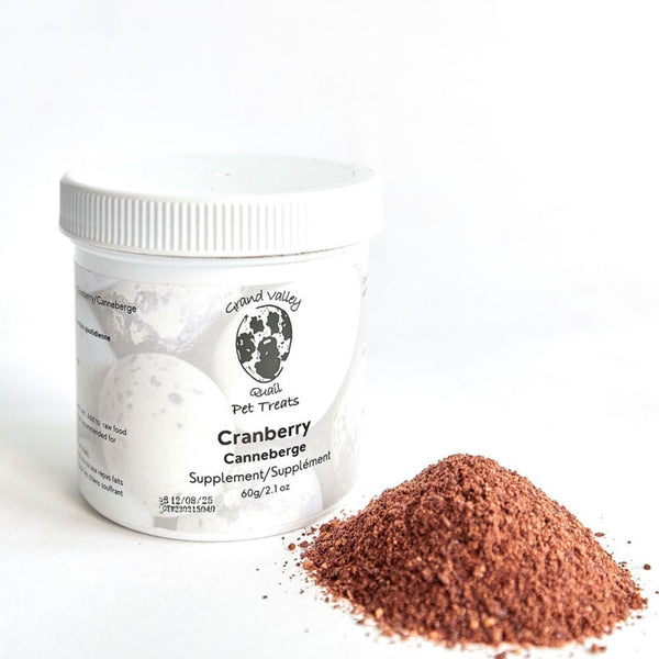 A white container of Grand Valley Quail Pet Treats cranberry supplement for dogs, placed next to a small pile of fine cranberry powder. The label highlights its natural ingredients and use as a dietary supplement.