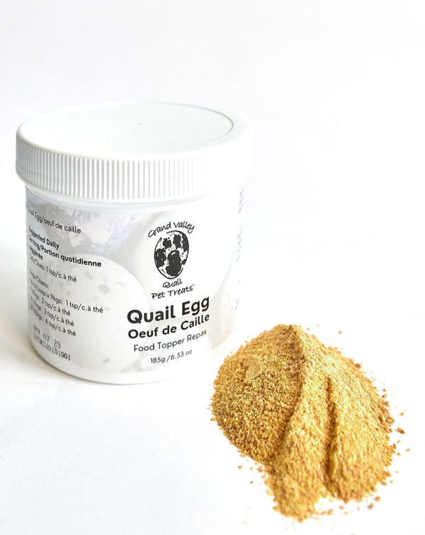 A white container of Grand Valley Quail Pet Treats quail egg food topper for dogs, placed beside a small pile of fine golden powder. The label highlights its nutritional benefits and use as a meal enhancer.